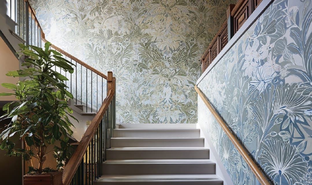 Interior photo of a sundrenched stairwell with a blue botanical pattern printed on the walls